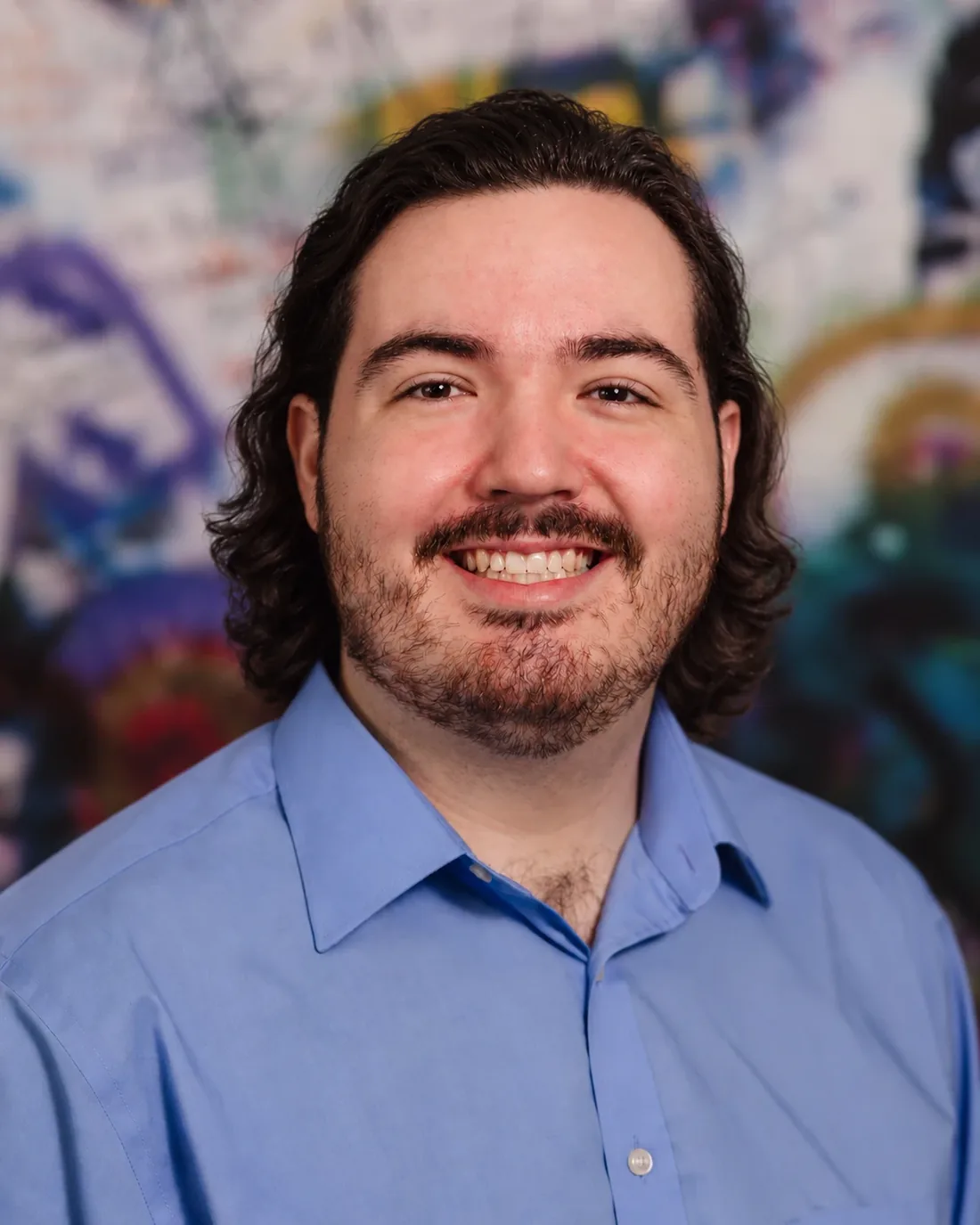 Portrait of Dan Garcia smiling in a blue shirt in front of a colorful graffiti wall