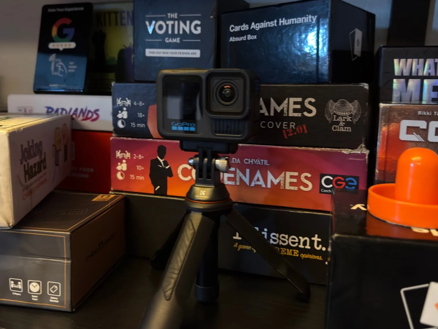 GoPro HERO13 Black mounted on a small black tripod in front of a stack of board games