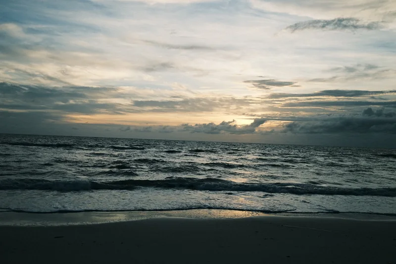 Waves rolling onto a beach under a cloudy sky as the sun sets over the Gulf in Naples, Florida